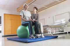 Physical therapist with patient balancing on ball.