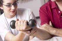 Patient using dumbells to exercise arm with physical therapist